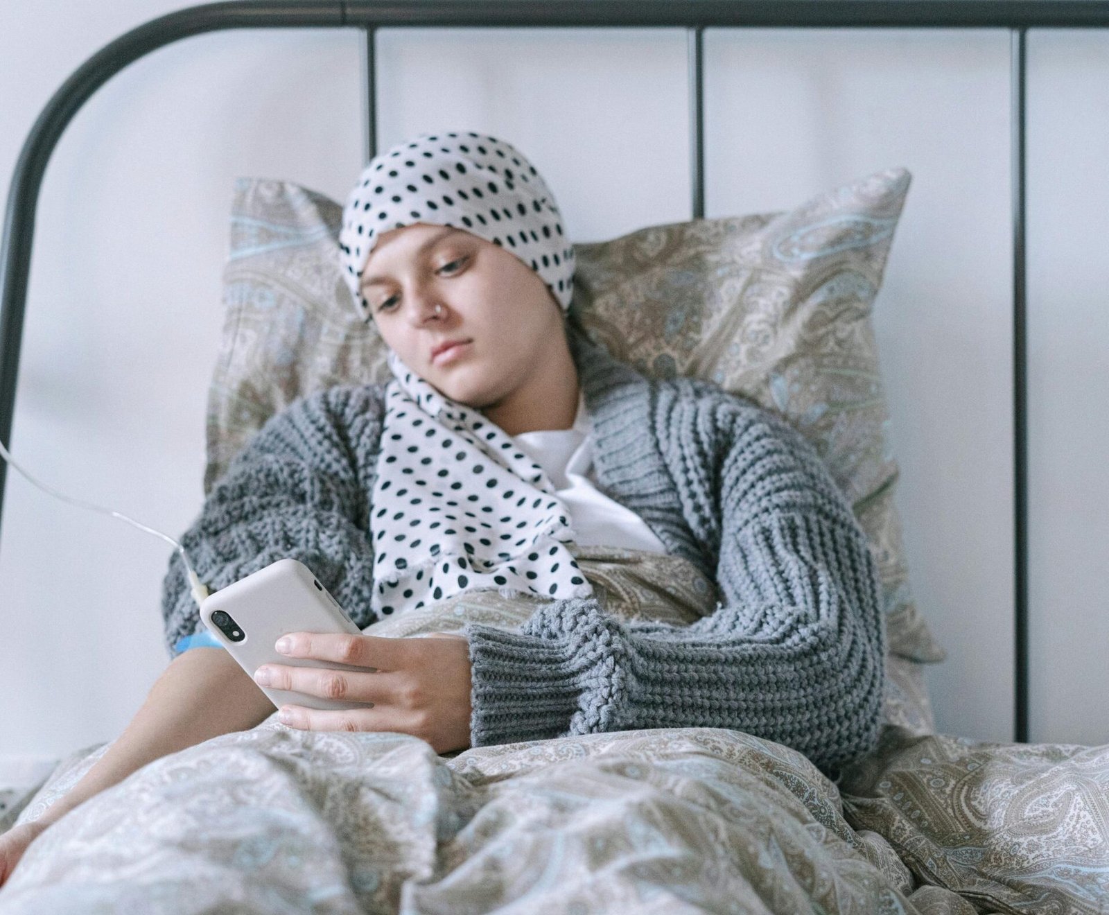 An ill woman with a head scarf using a smartphone, lying in bed, symbolizing hope and recovery.